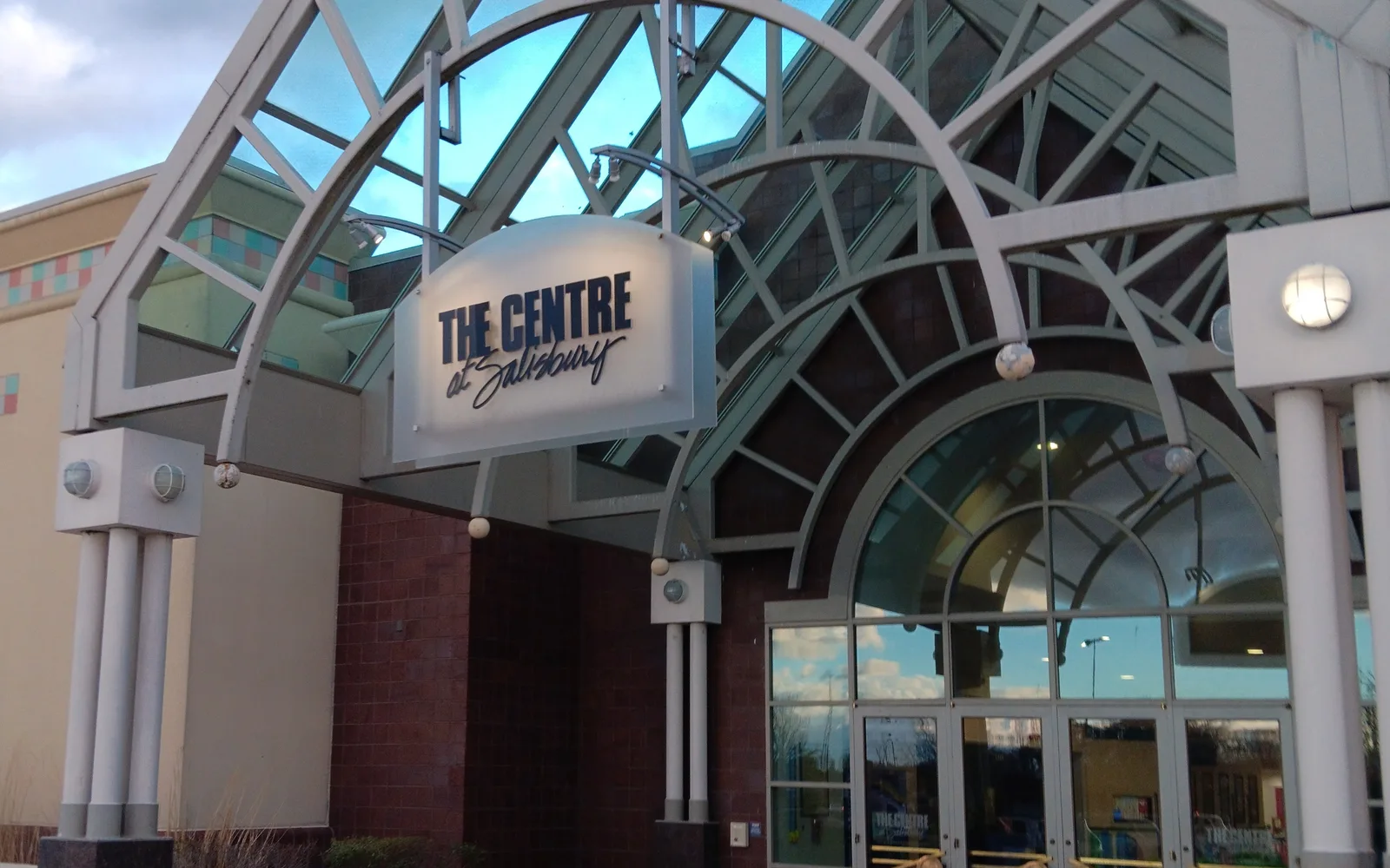 The main entrance to a shopping center with glass doors and signage, showing the architectural facade of a retail complex
